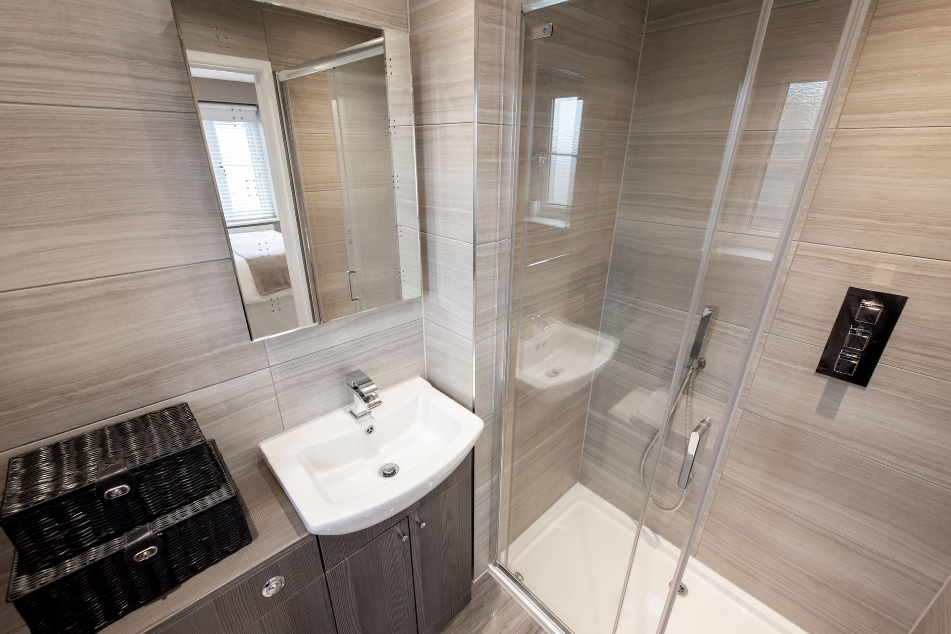 Small, modern bathroom with gray tiles, shower, sink, and mirror.