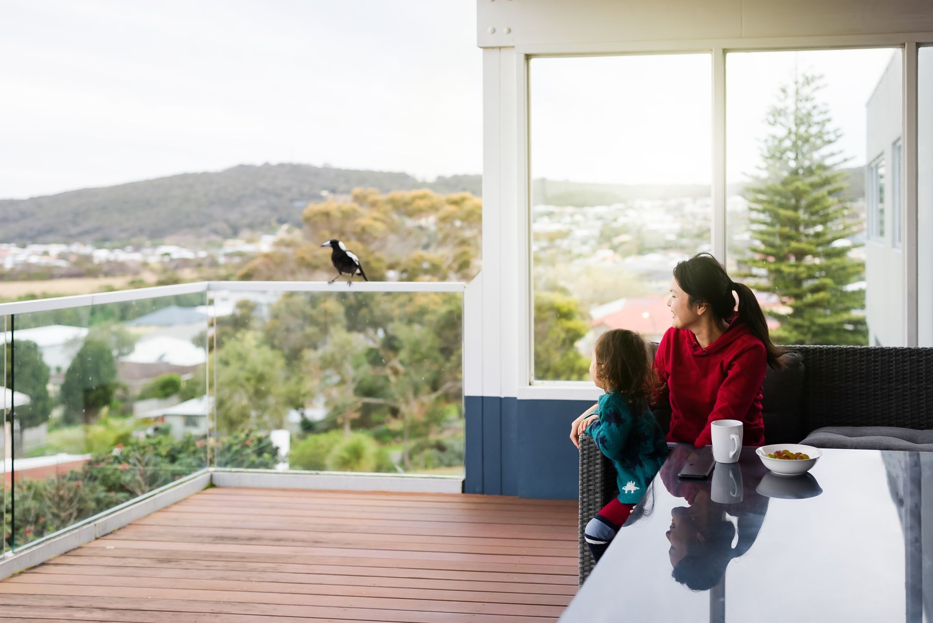 Person installing a window on a gray house using a drill, with a ladder nearby.