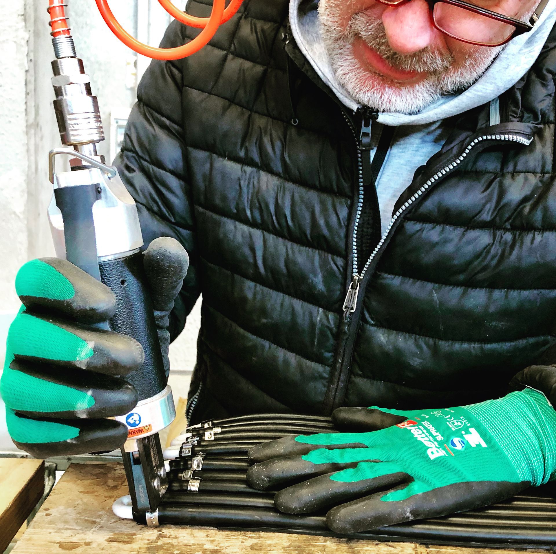 Un hombre que lleva una chaqueta negra y guantes verdes está trabajando en una pieza de metal.