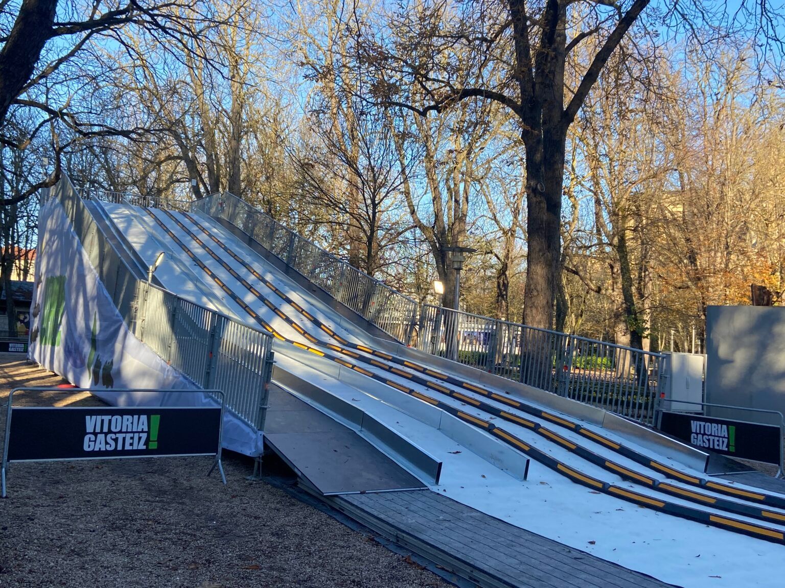 Se está construyendo un tobogán de nieve en un parque con árboles al fondo.