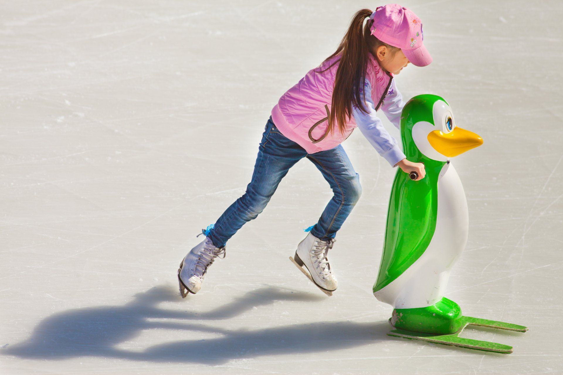 Una niña está patinando sobre hielo junto a una estatua de pingüino.