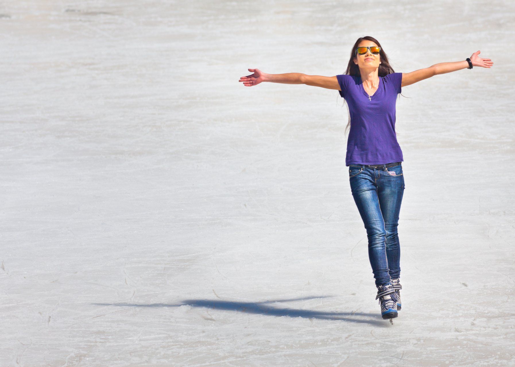 Una mujer con una camisa morada patina en una pista con los brazos extendidos.