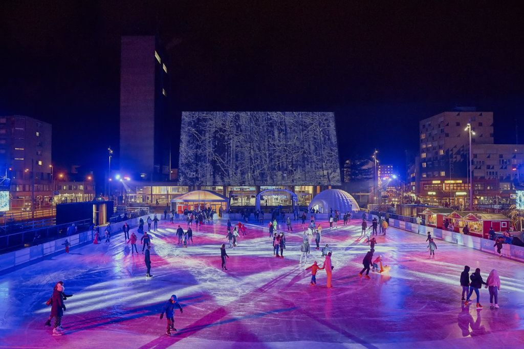 Una pista de hielo grande con iluminación y muchos patinadores al aire libre