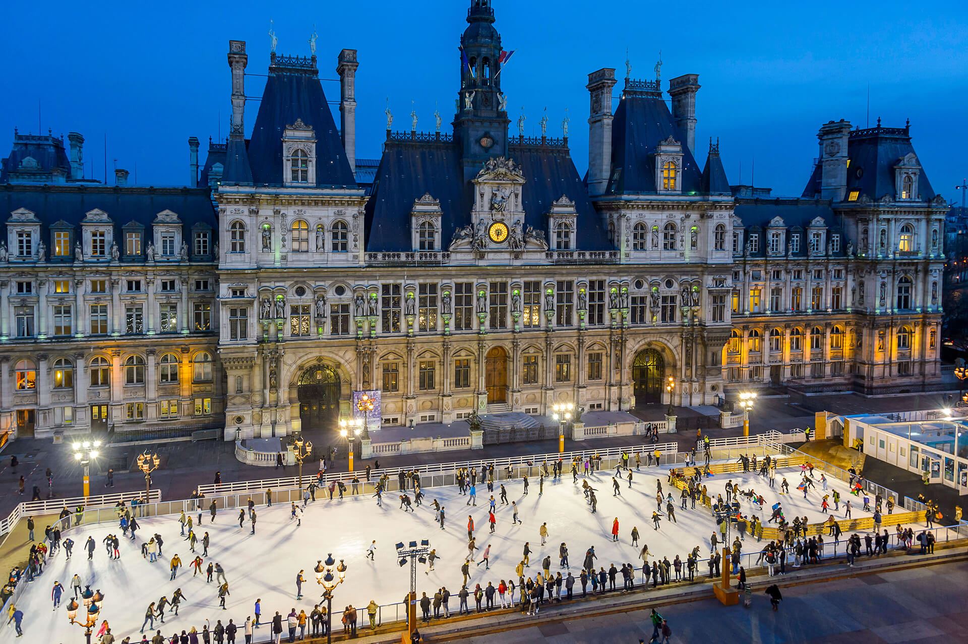 Una pista de hielo grande en centro urbano con muchas personas patinando sobre hielo
