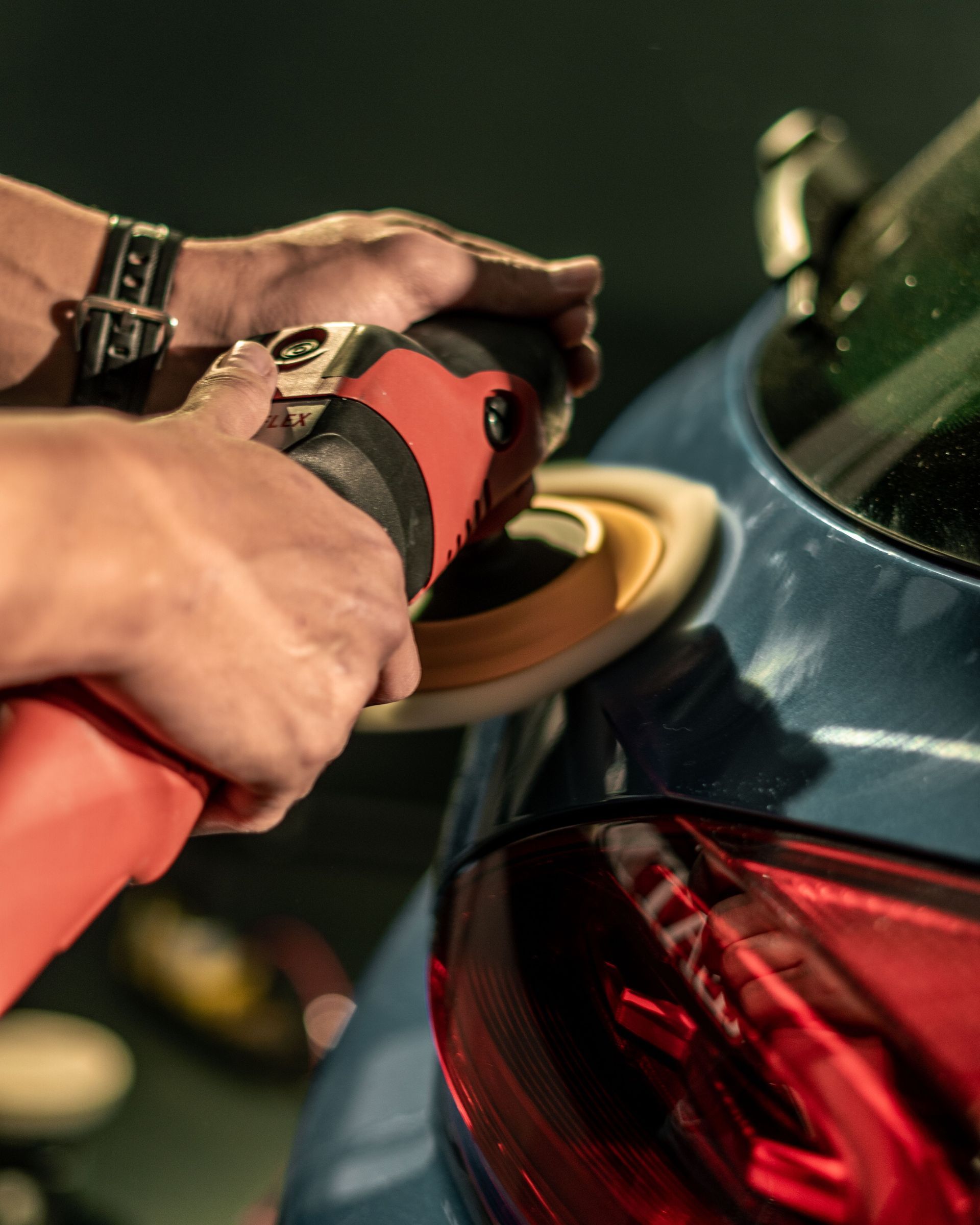 Man applying clear protective film to the hood of a black car in a workshop