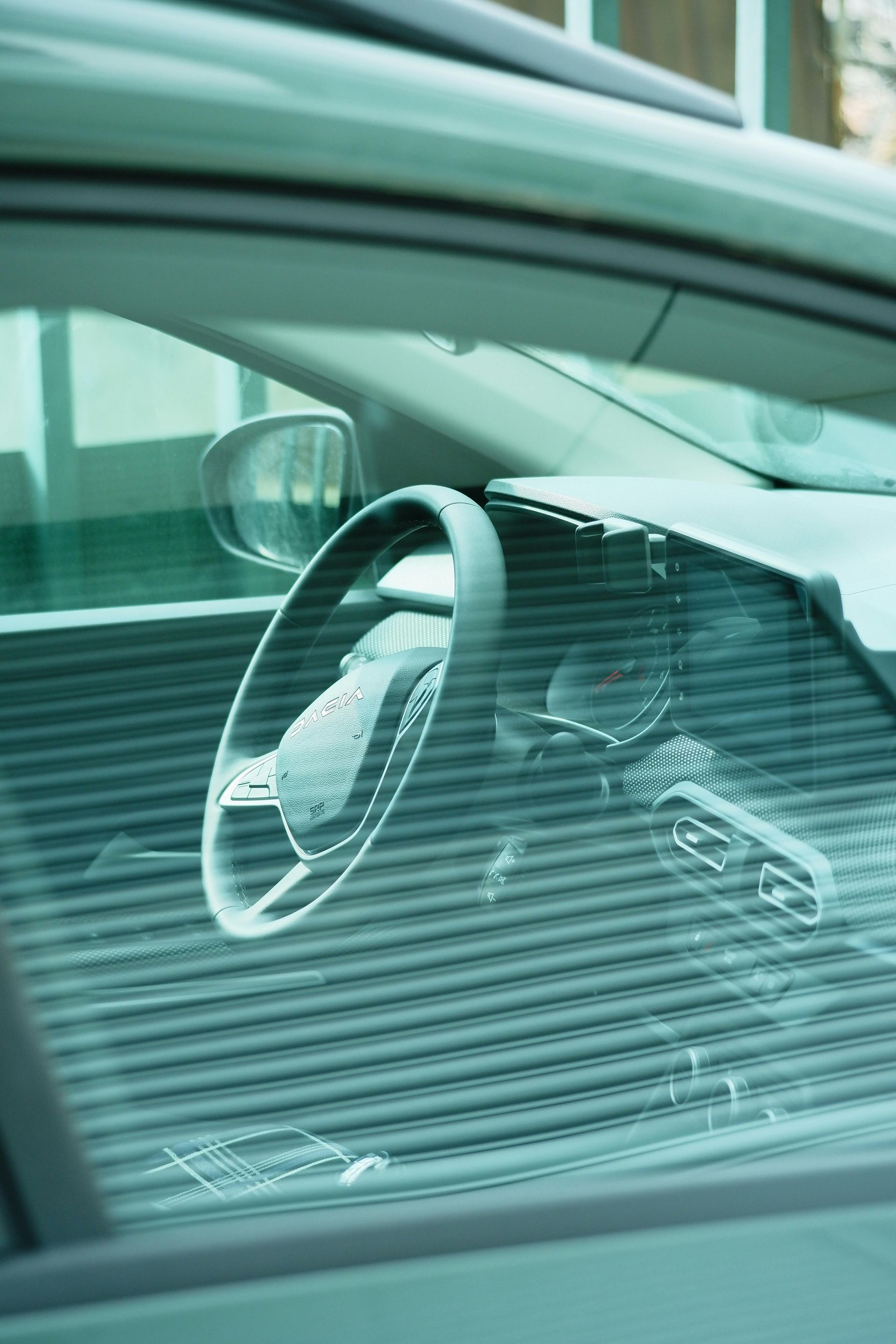 Close-up of the hood, windshield, and driver-side headlight of a dark grey sedan on a city street.