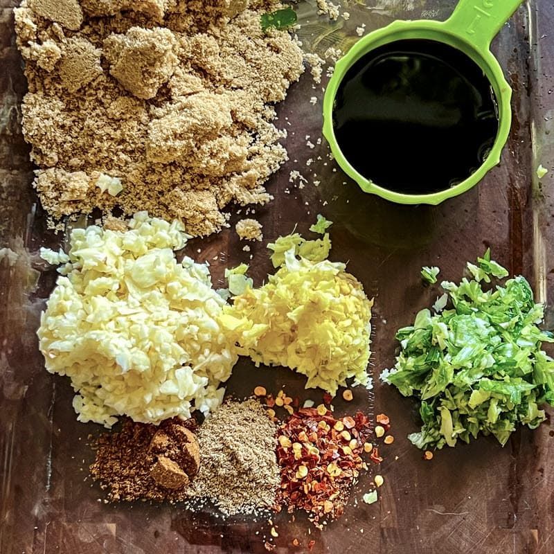 a table topped with bowls of various spices including brown sugar, chili flakes, soy sauce, minced ginger