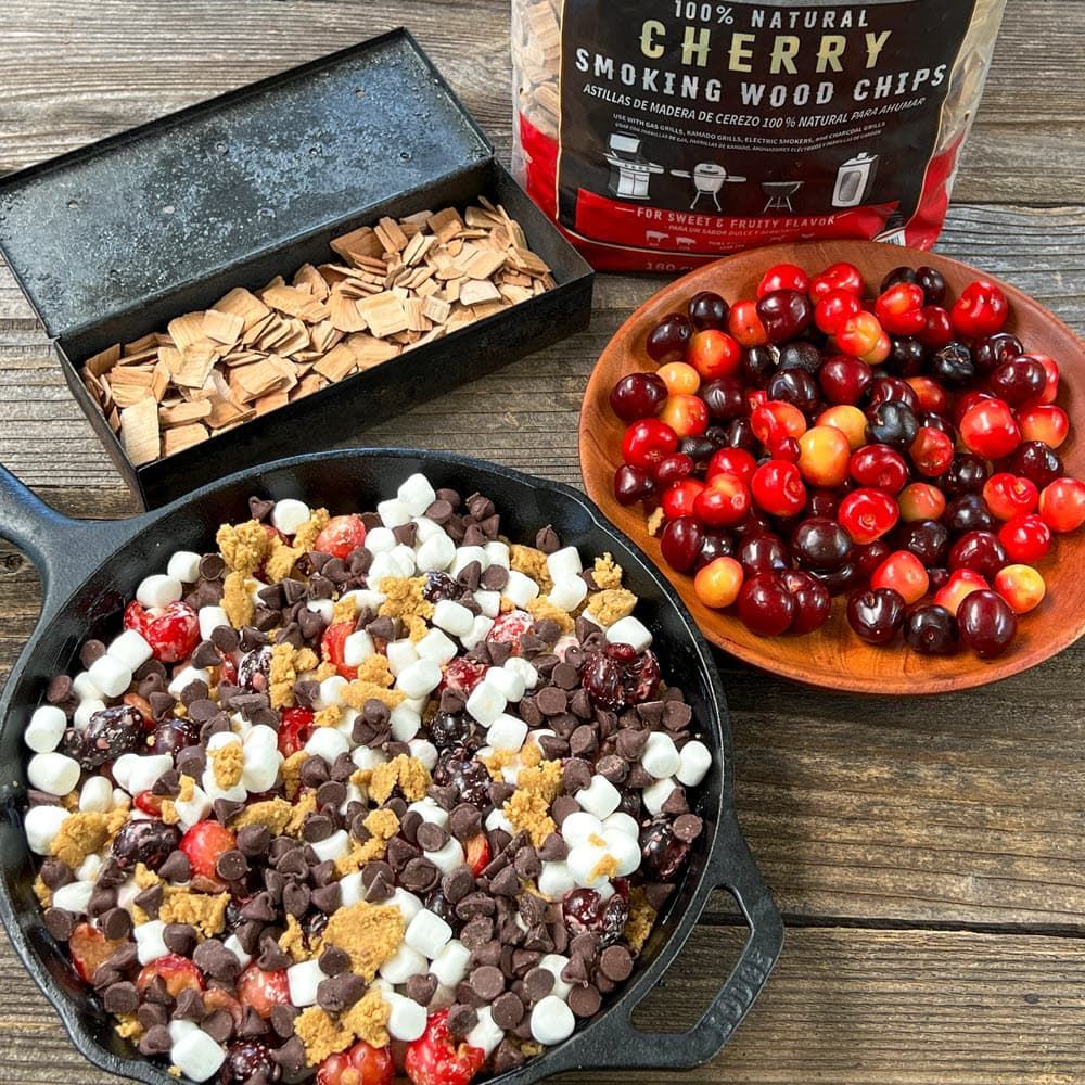 cast iron pan of chocolate cherry s'mores dessert with a bowl of  cherries