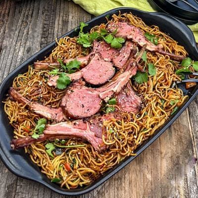 A cast iron pan filled with noodles and grilled lamb chops.