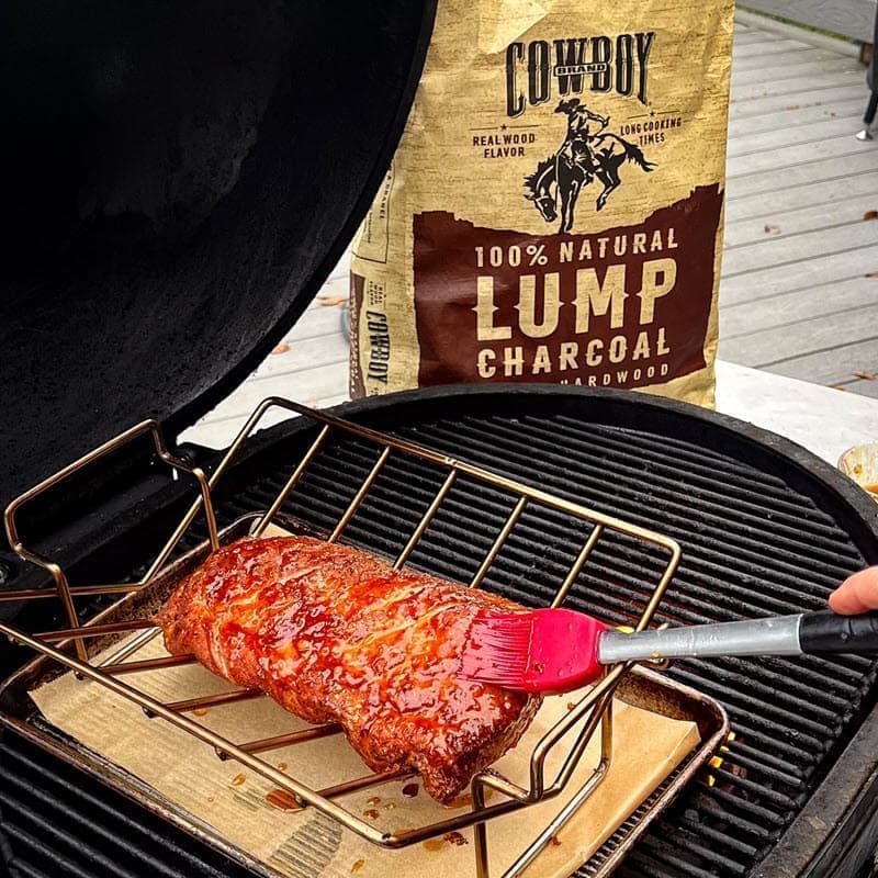A glazed pork loin is cooking on the grill with a bag of cowboy lump charcoal in the background