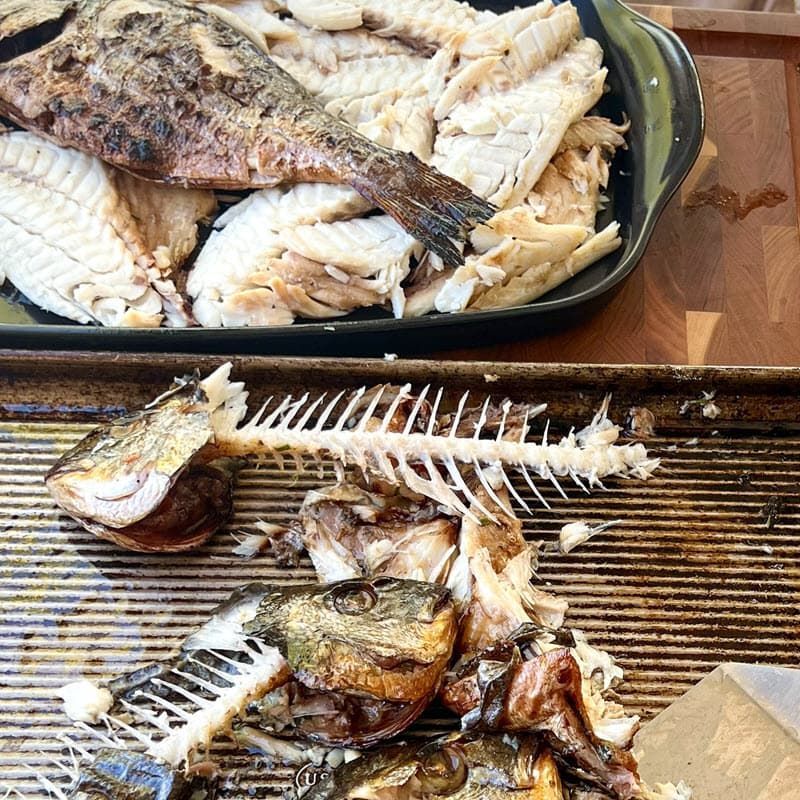 A tray of fish and a tray of fish bones on a table.