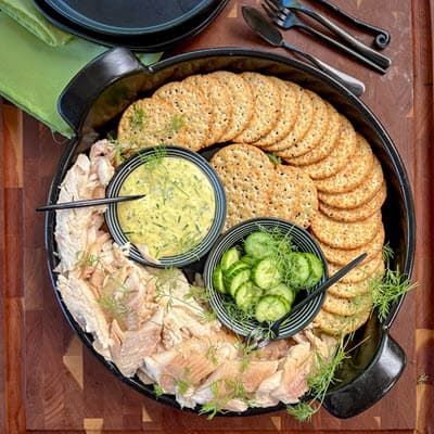 A pan filled with crackers , fish, cucumbers and mustard dill dip