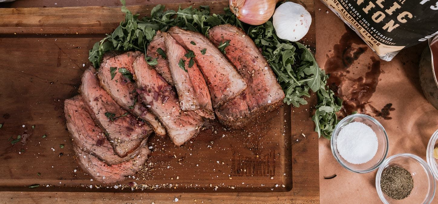a wooden cutting board topped with sliced sirloin steak with garnish.