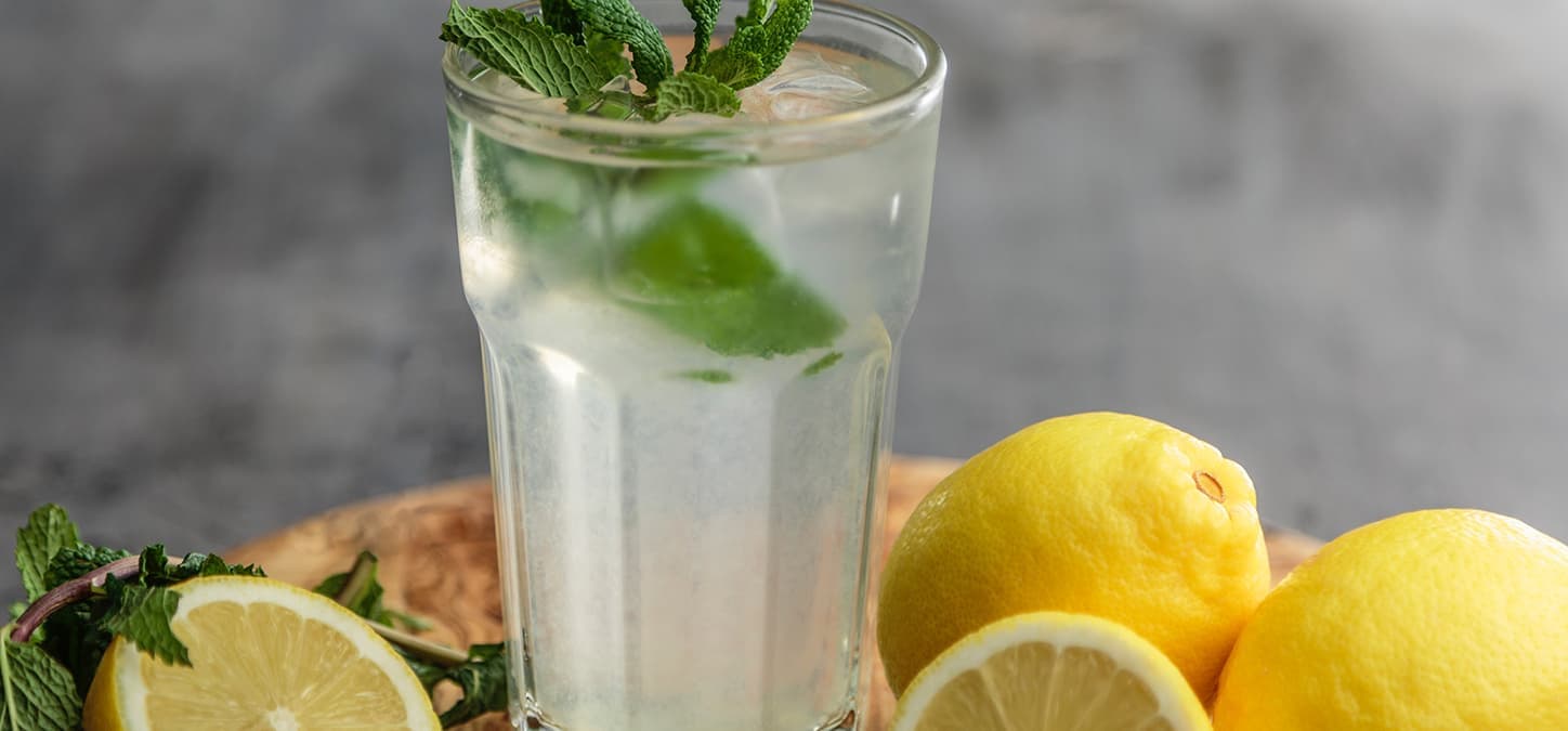 Grilled basil lemonade with ice in tall glass surrounded by lemons