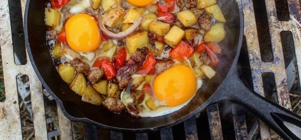 Potatoes, bell peppers, onions and fried eggs in a skillet cooking over live fire