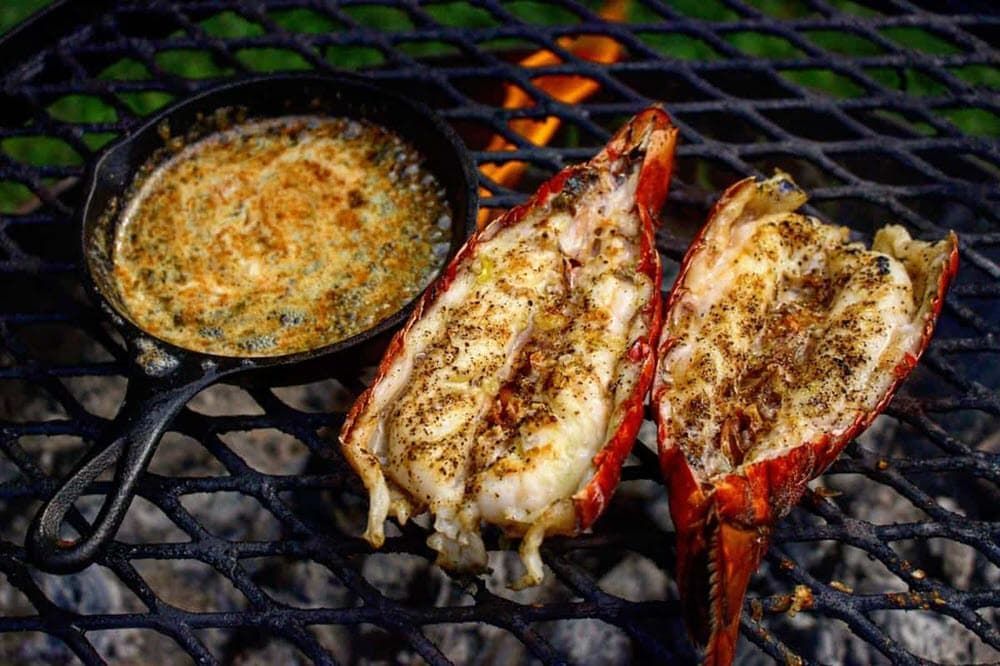 lobster tails in their shells  and  chive butter sauce in a cast iron grill cooking on the grill