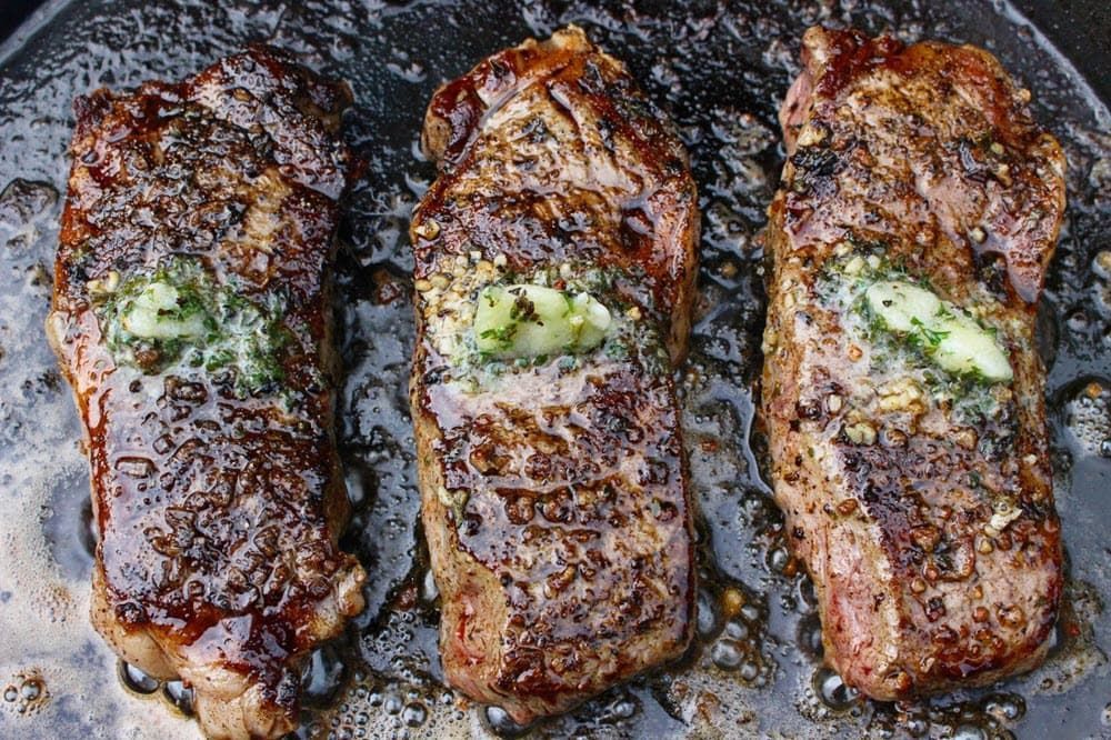 3 grilled herb butter steaks sizzling on iron cast pan
