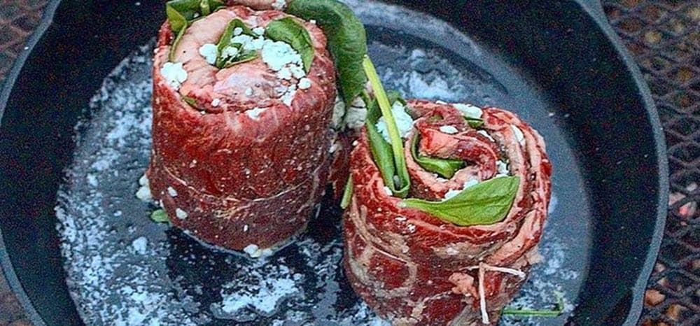 skirt steak rolled into pinwheels in a cast iron pan cooking over the grill