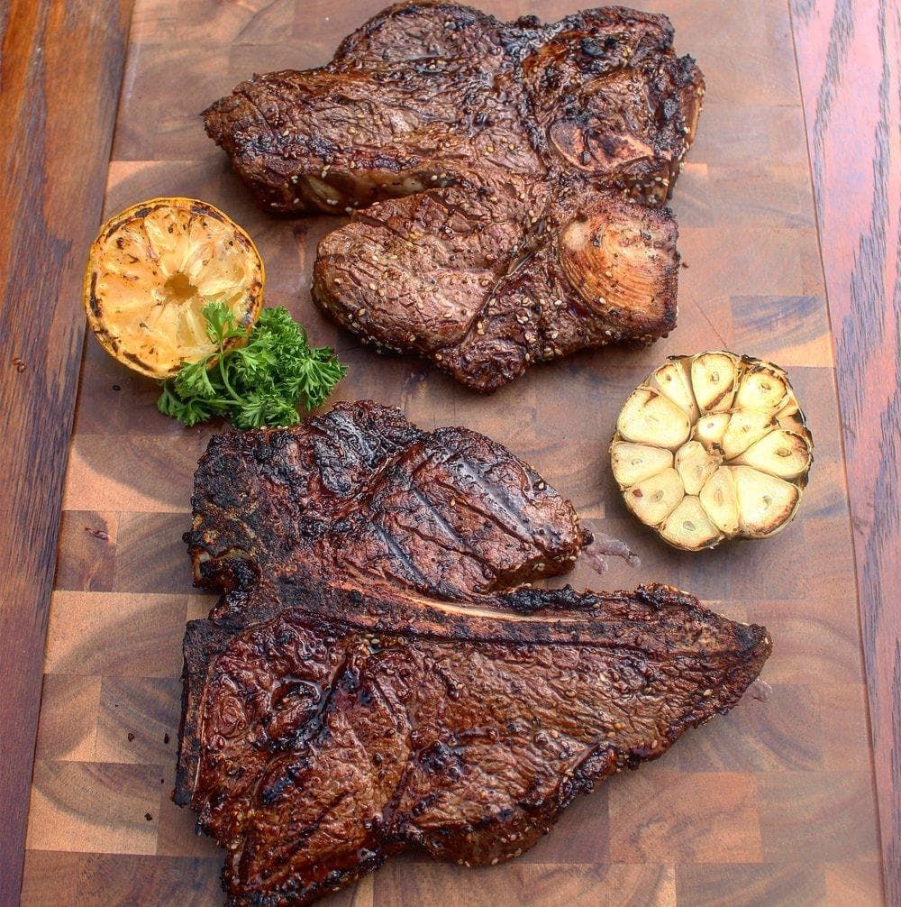 Porterhouse steaks on cutting board with grilled lemon and garlic