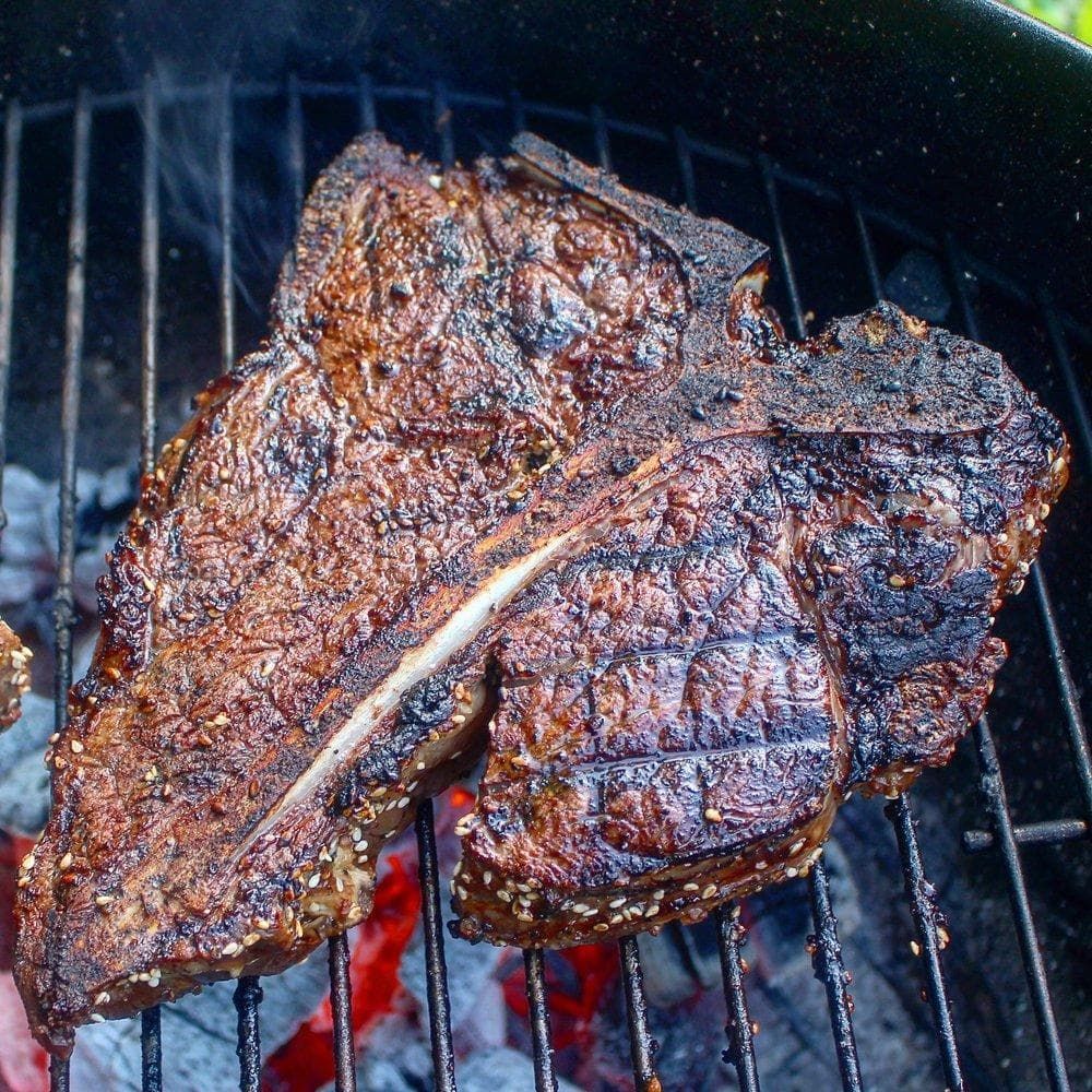 Charred porterhouse steak cooking on a grill over glowing coals