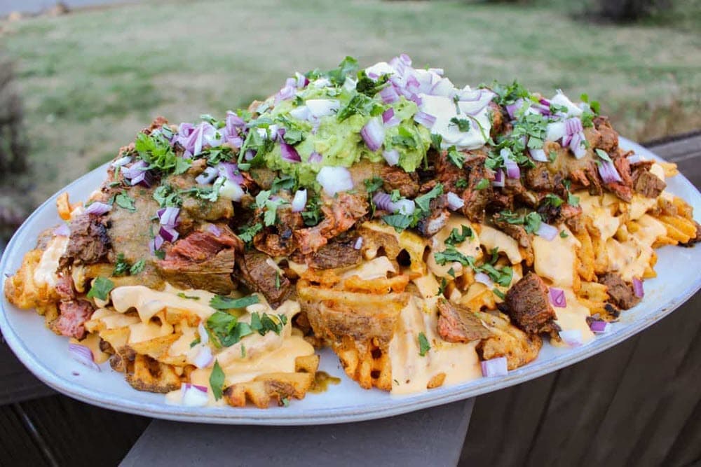 platter of waffle fries topped with grilled steak, guacamole, cheese and onions