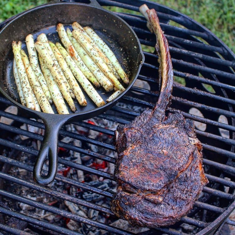 Tomahawk Steak and white asparagus in iron pan cooking on the grill