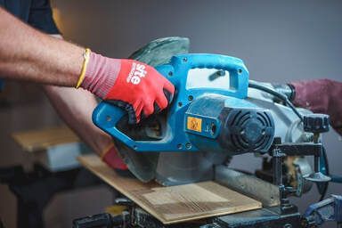 Picture of a handyman cutting flooring boards with a blue chop saw.