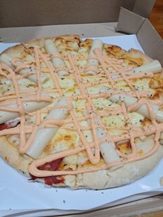 Pizza servida en una caja de cartón con un chorrito de salsa de naranja y trocitos de ingredientes.