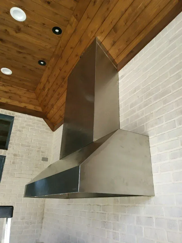 A stainless steel hood is hanging from the ceiling of a kitchen.