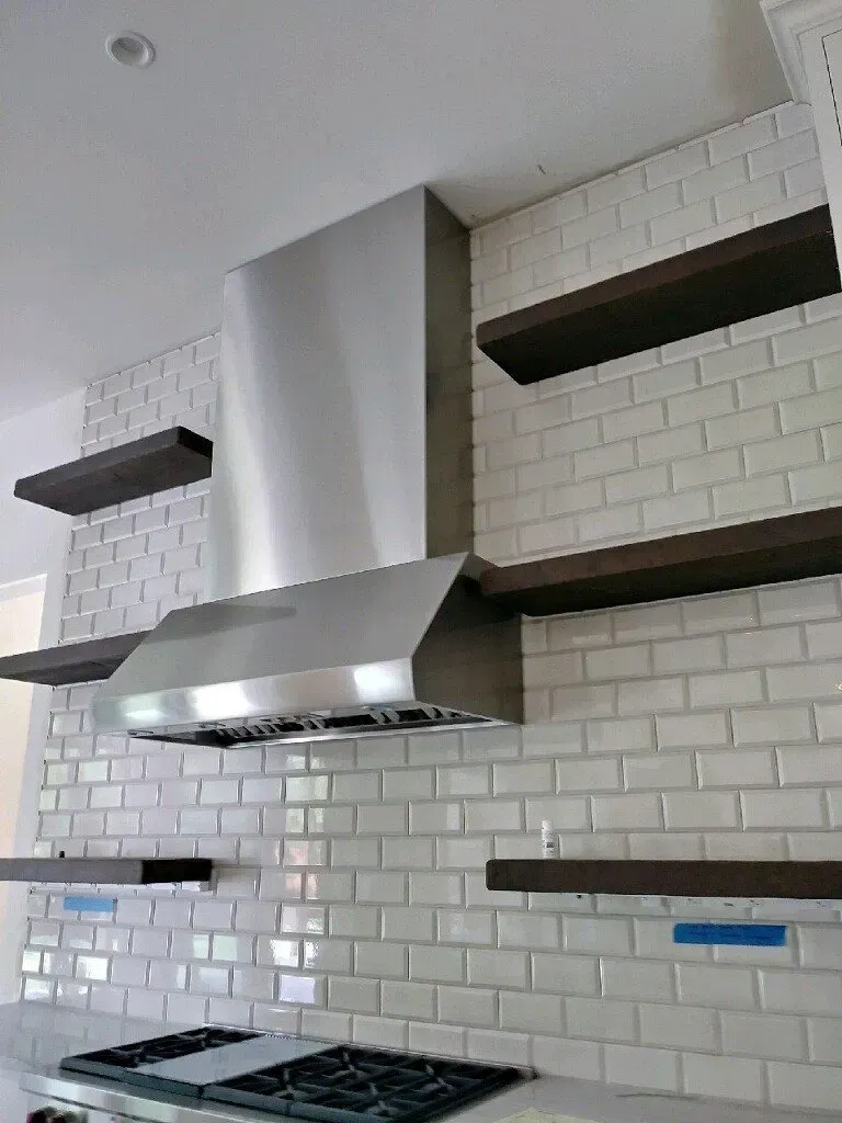A kitchen with white brick walls , stainless steel appliances , and wooden shelves.