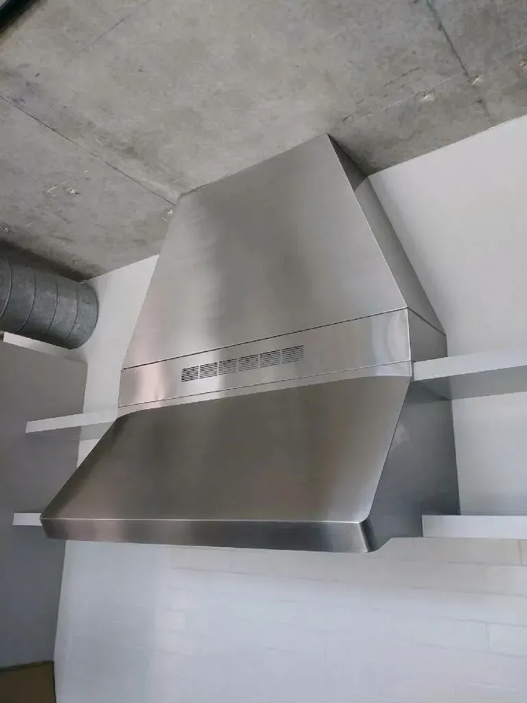 A stainless steel hood is hanging from the ceiling in a kitchen.