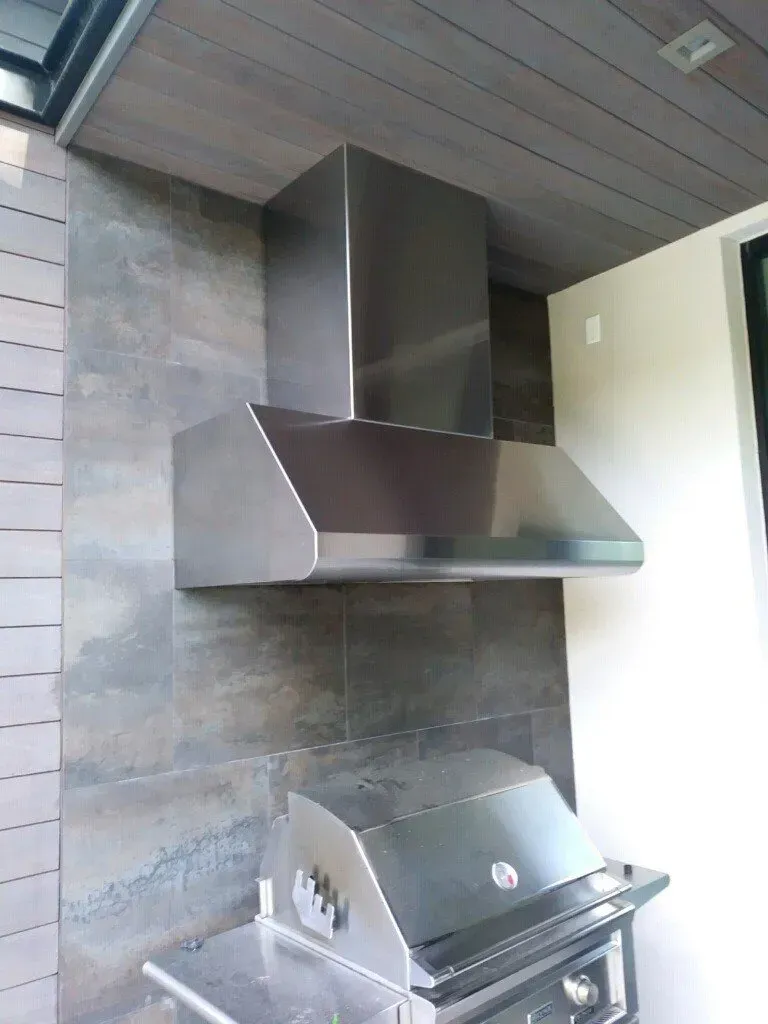 A stainless steel hood is hanging from the ceiling above a grill.