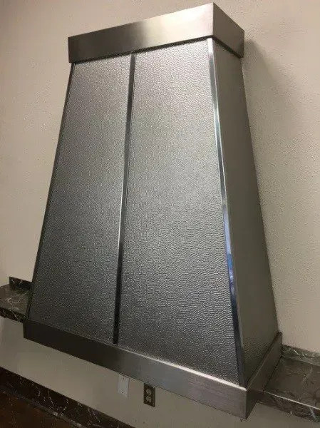 A stainless steel hood is hanging on a wall in a kitchen.