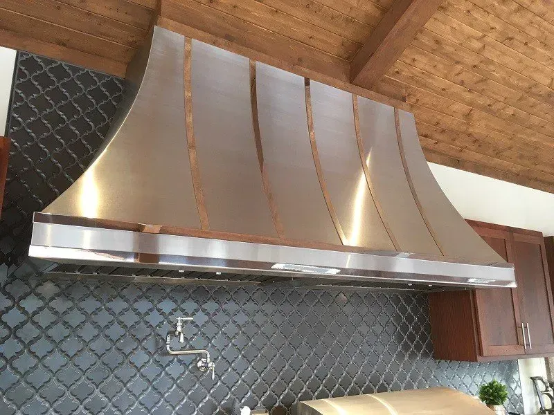 A stainless steel hood is hanging from the ceiling in a kitchen