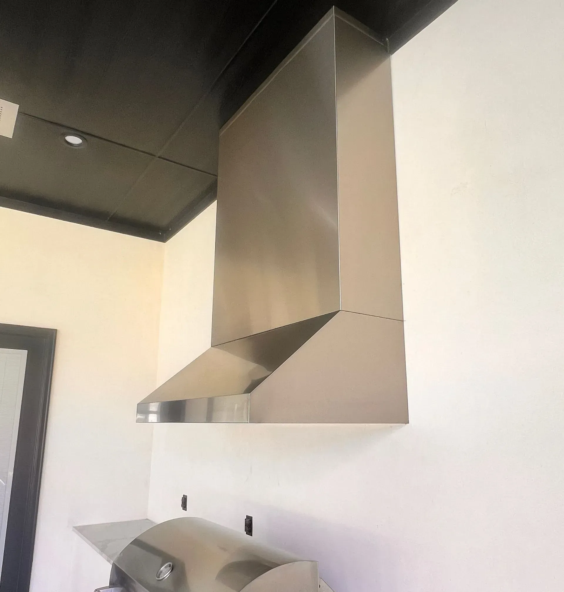 A stainless steel hood is hanging from the ceiling in a kitchen