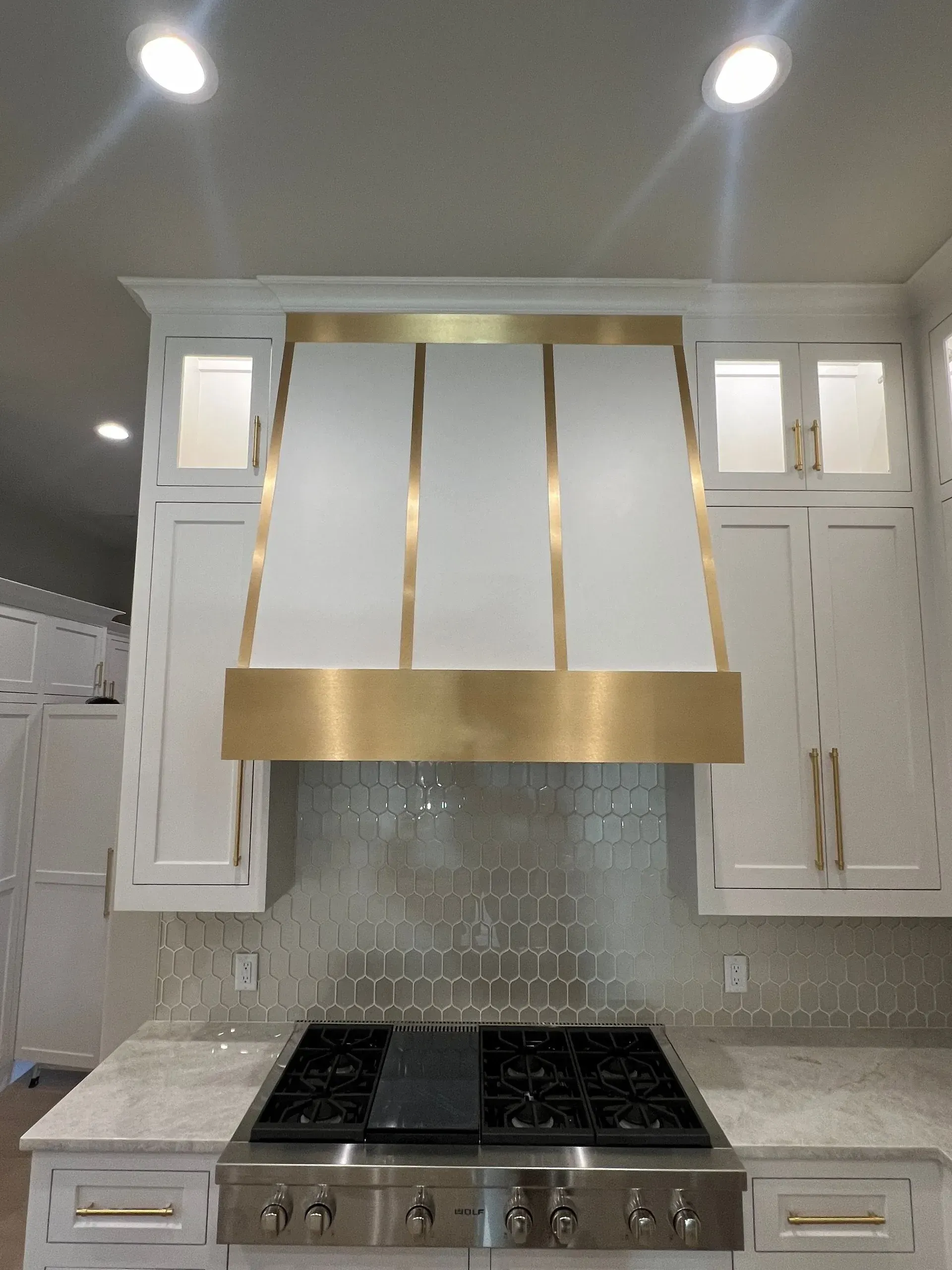A kitchen with white cabinets and a brass hood over the stove