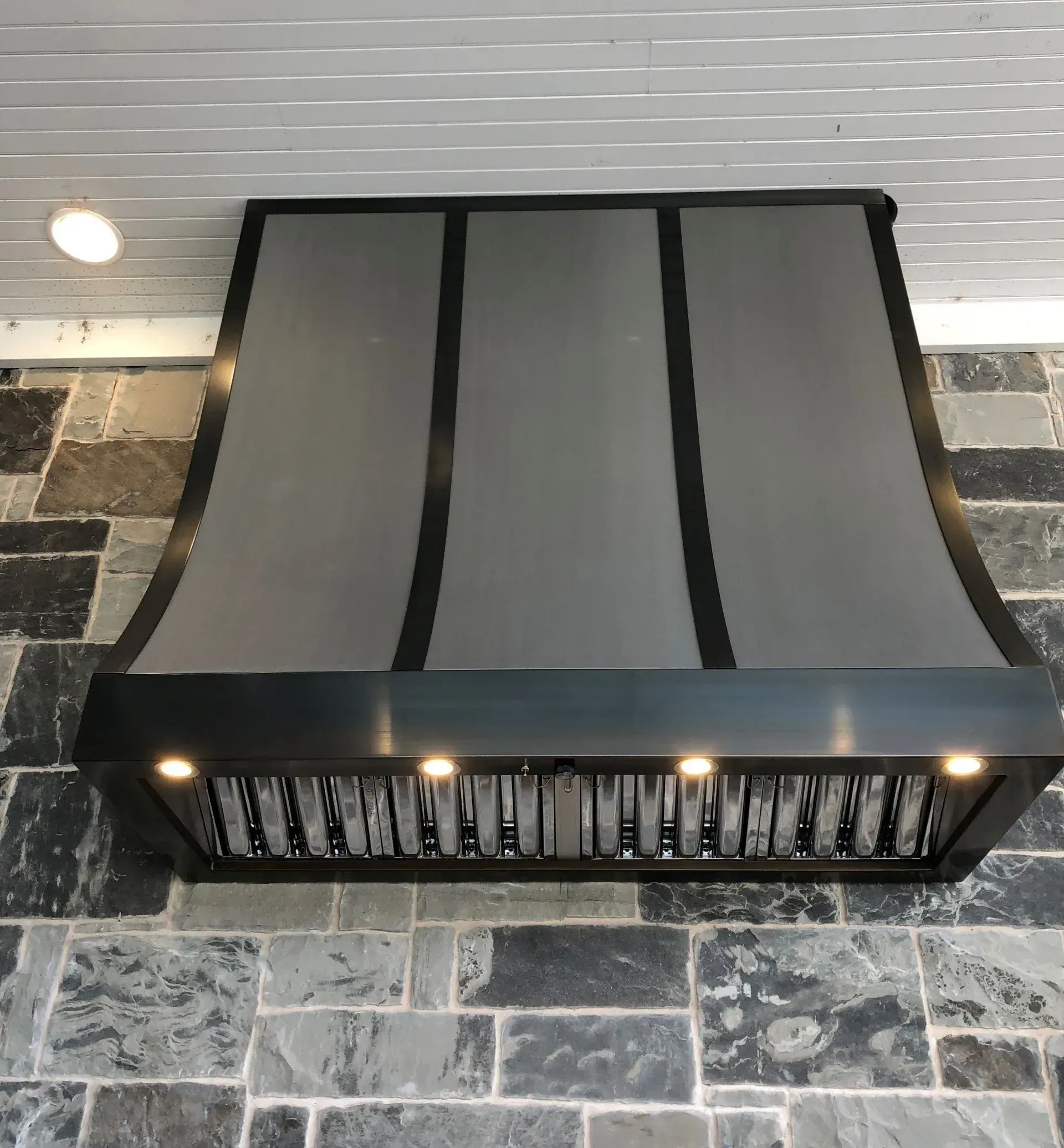 A stainless steel hood is hanging on a brick wall