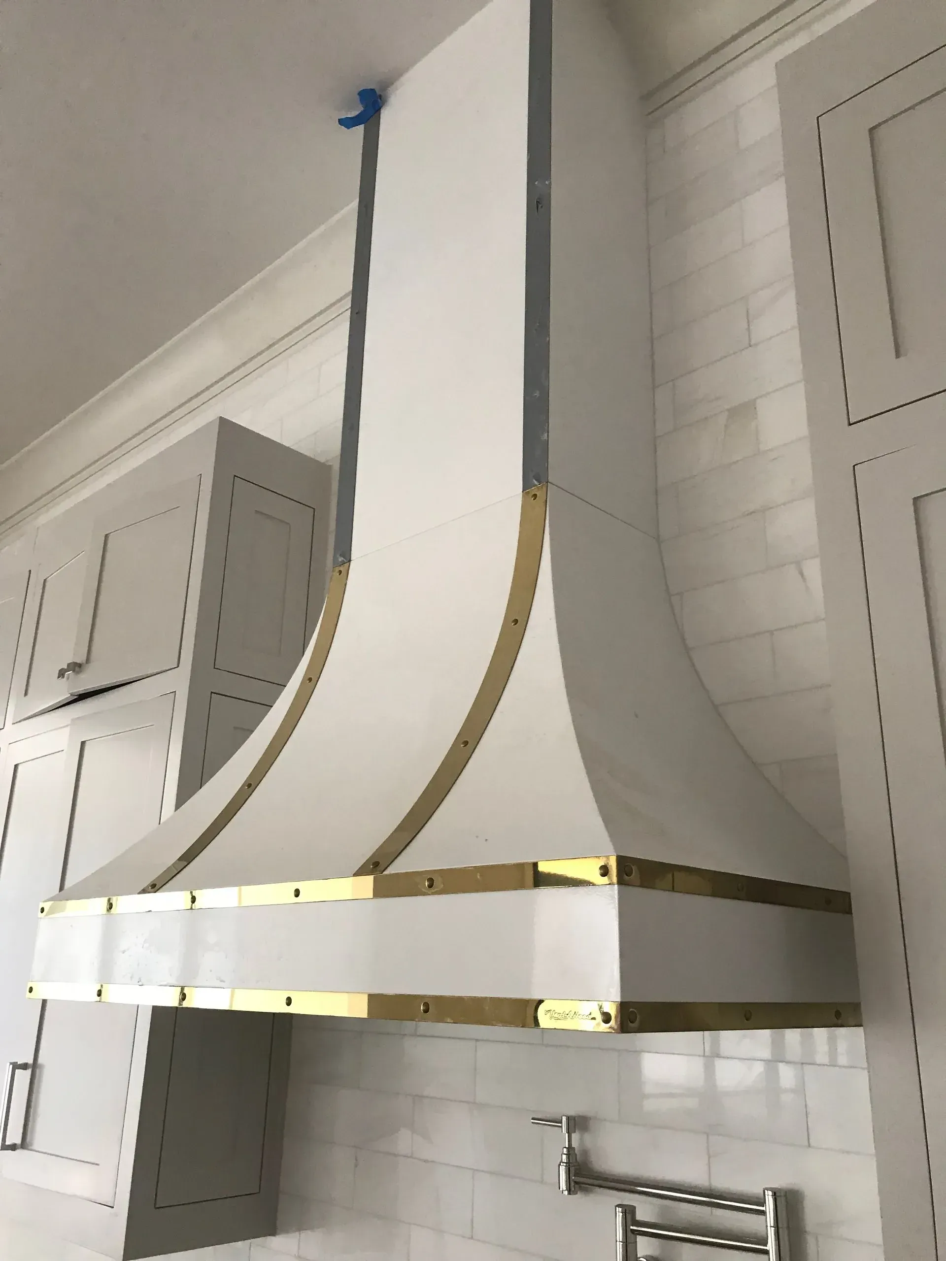 A white hood with gold trim is hanging from the ceiling in a kitchen
