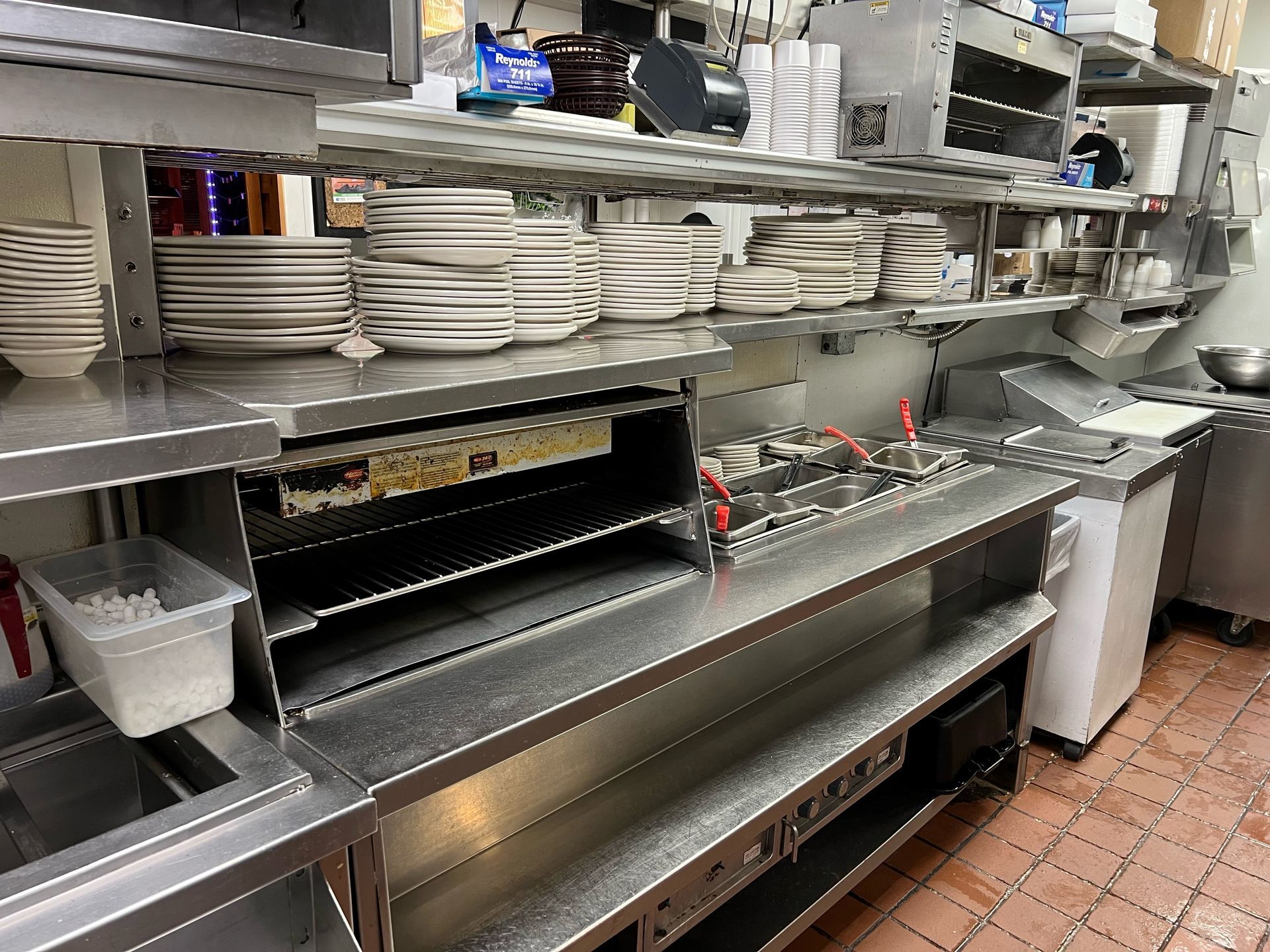 A kitchen with a lot of stainless steel appliances and plates on the shelves.
