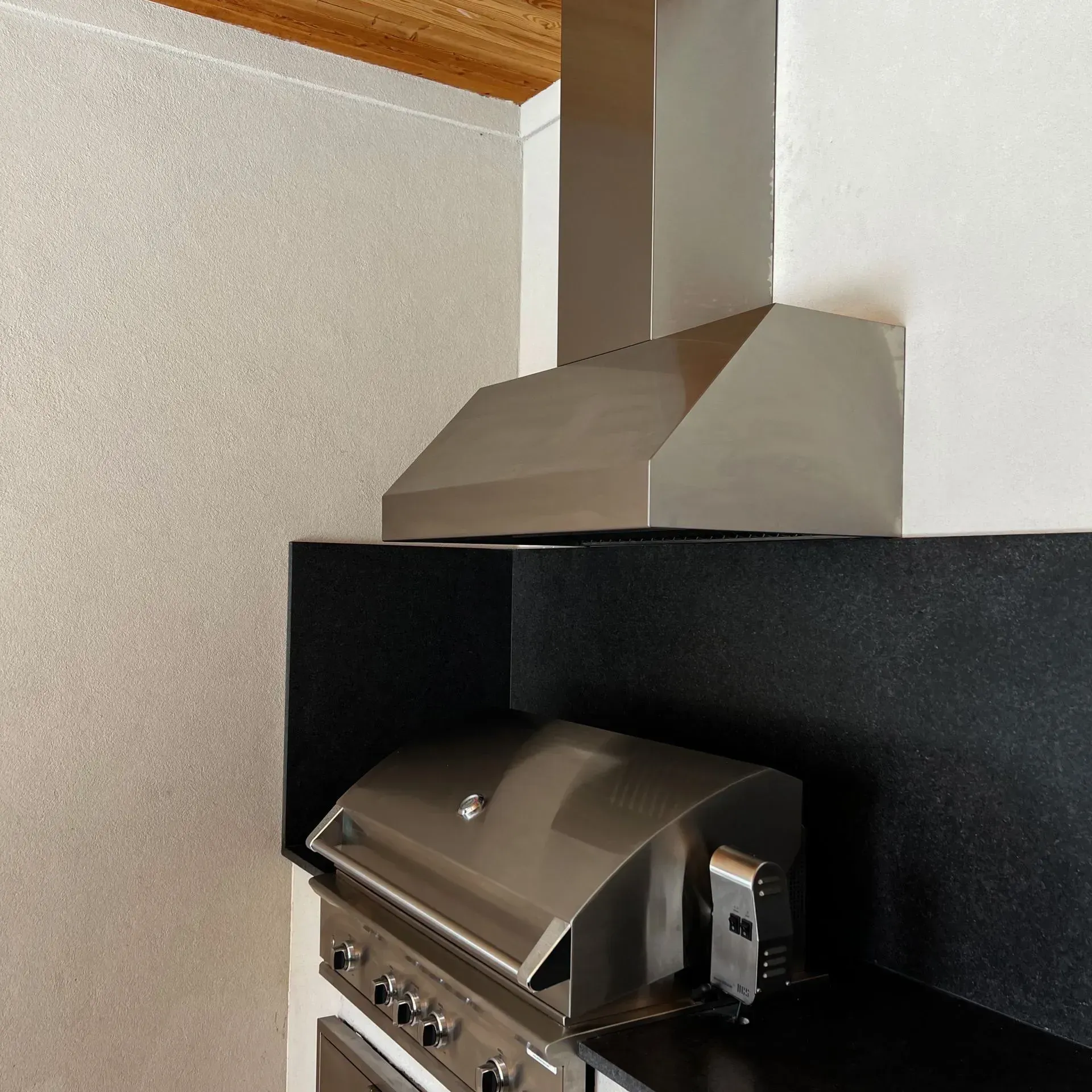 A stainless steel grill is sitting under a hood in a kitchen