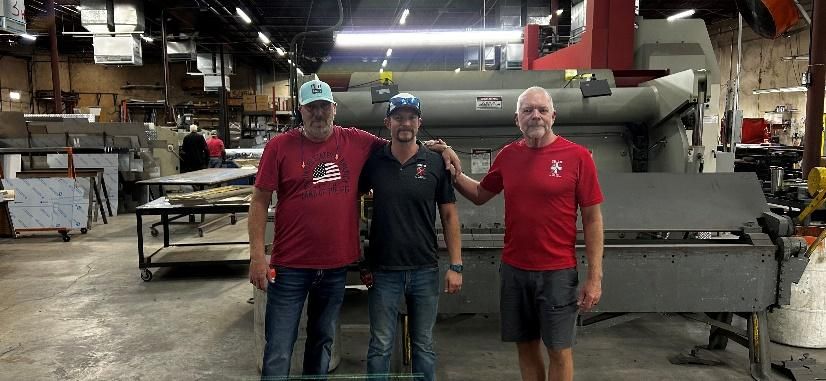 Three men are posing for a picture in a factory.