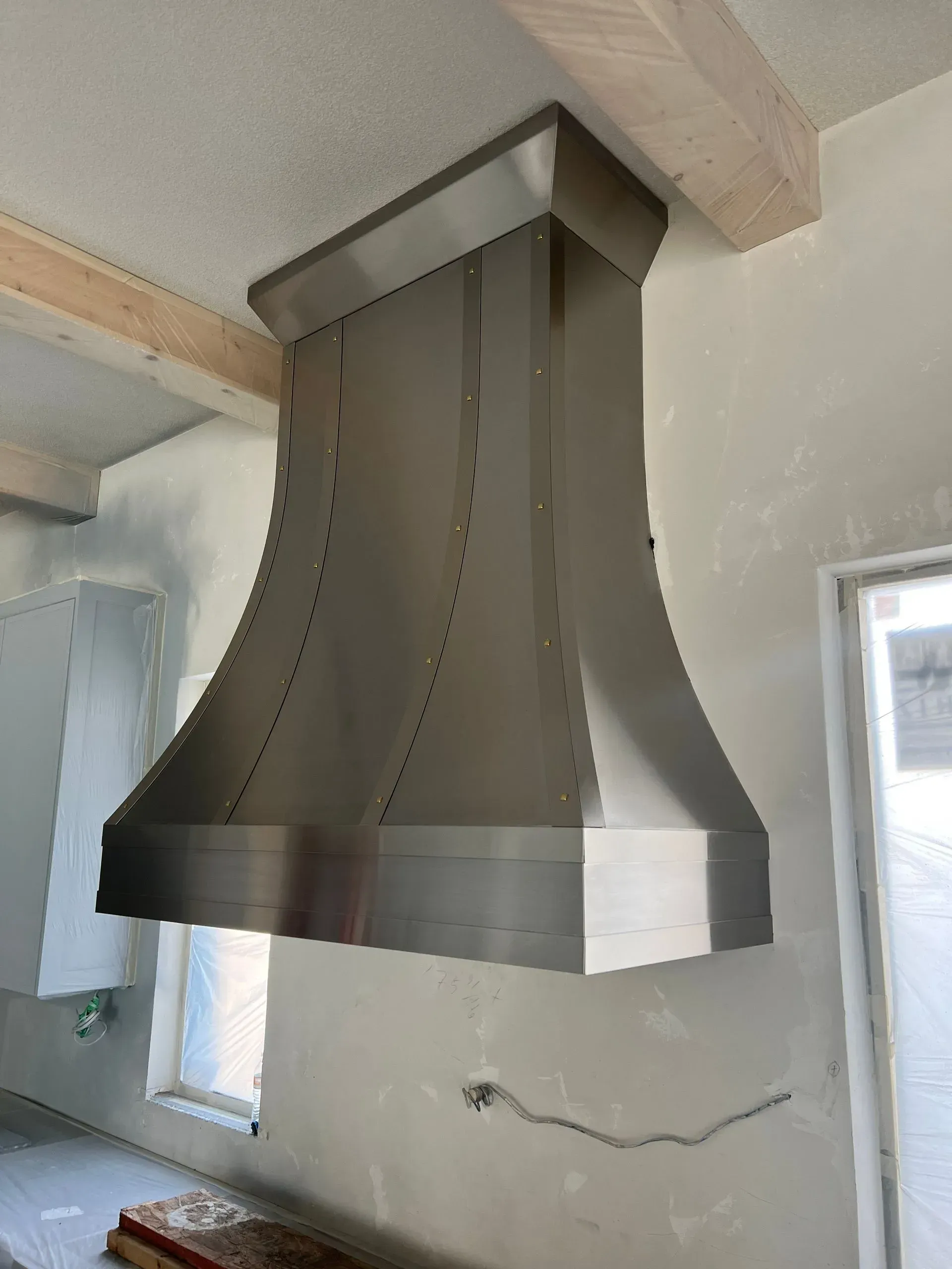 A stainless steel hood is hanging from the ceiling in a kitchen.