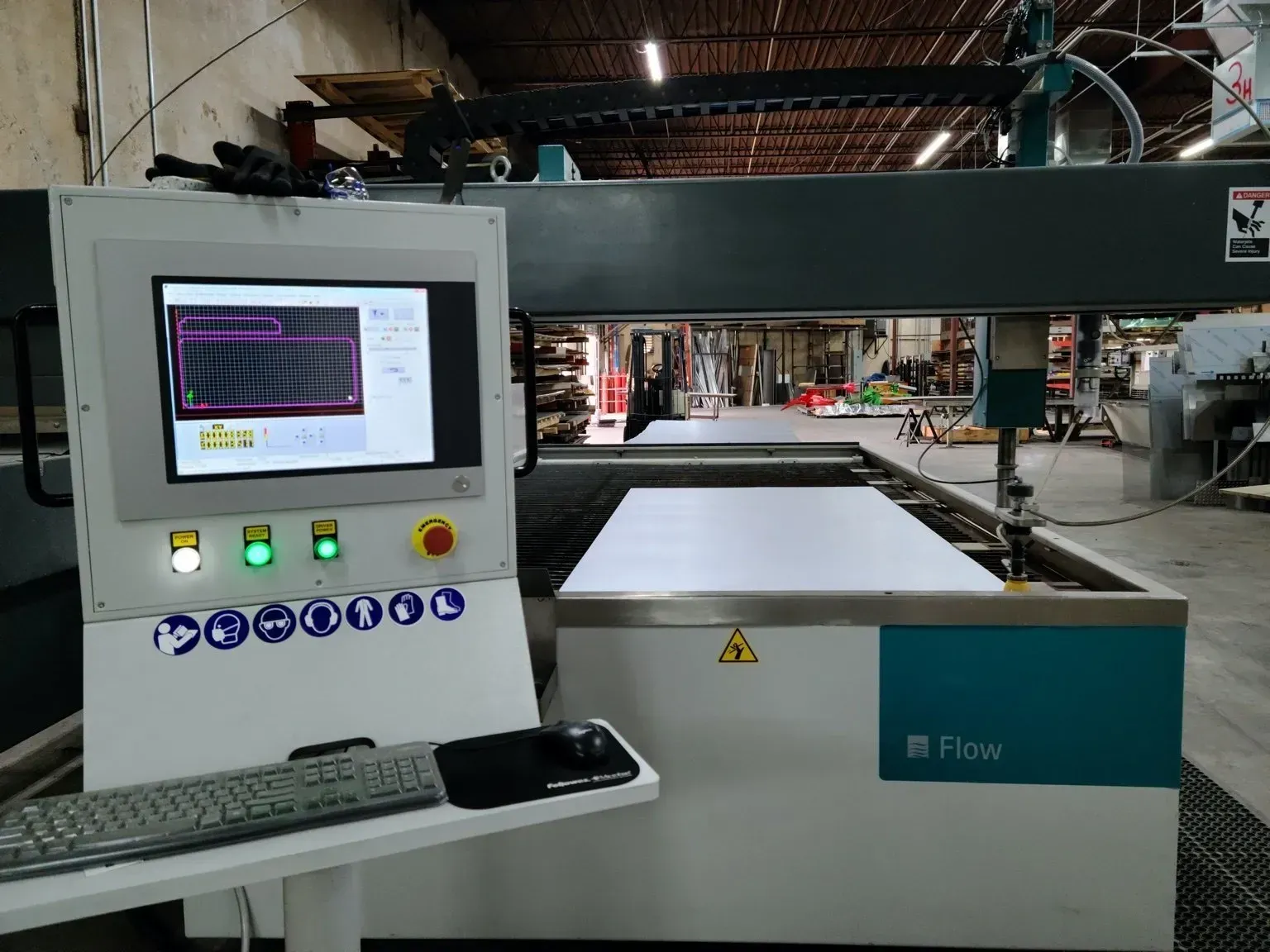 A computer monitor is sitting next to a machine in a warehouse.