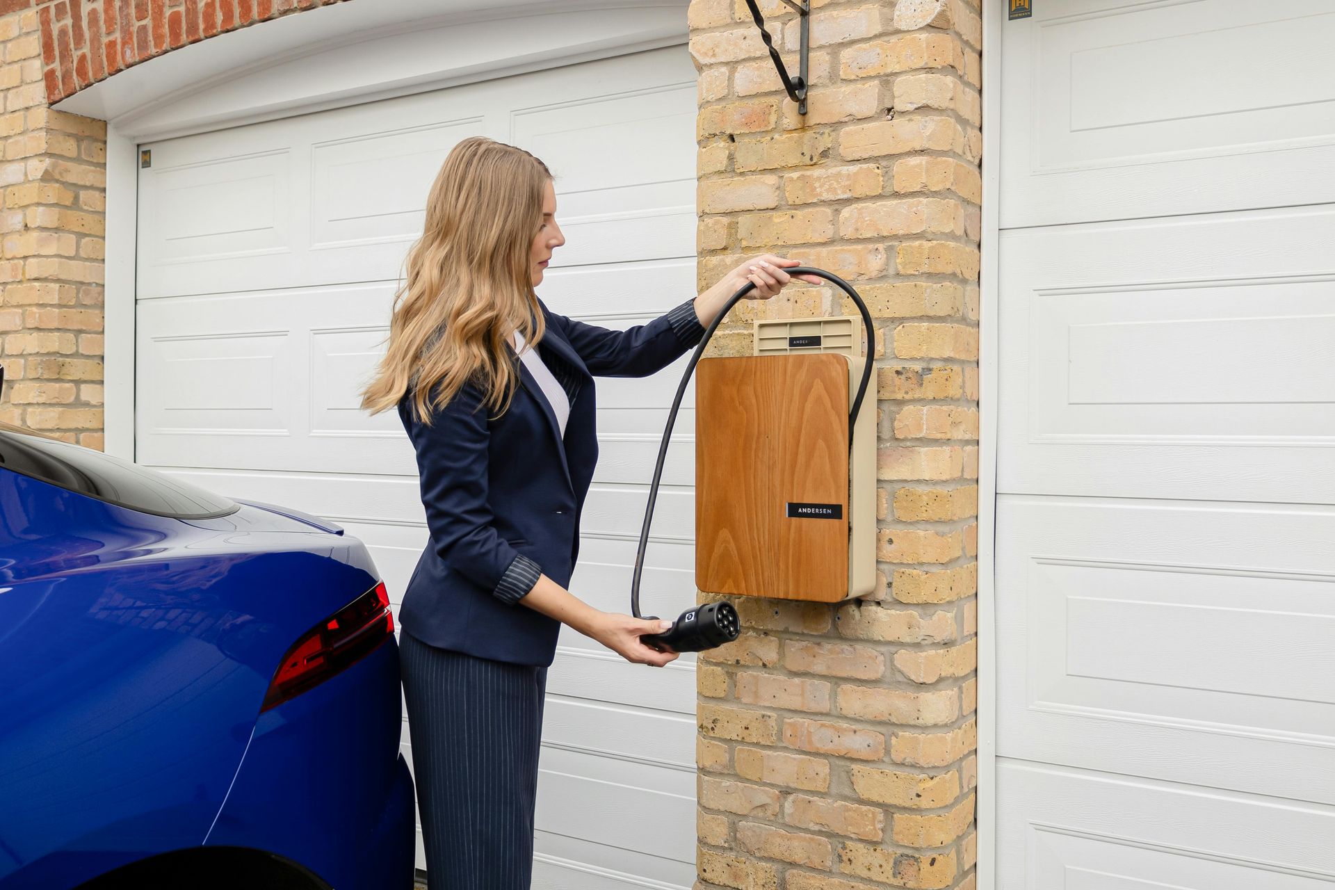 Woman plugging electric car charger into an electric vehicle outside a garage.