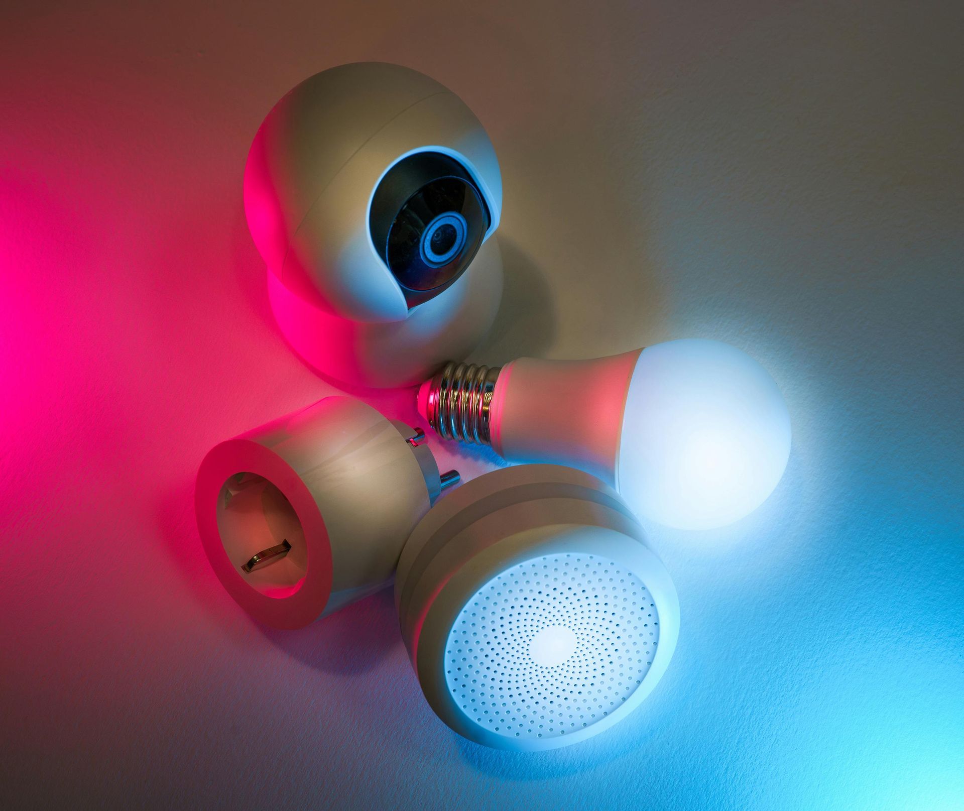 Smart home devices, including a camera, light bulb, and speaker, glow with pink and blue light.
