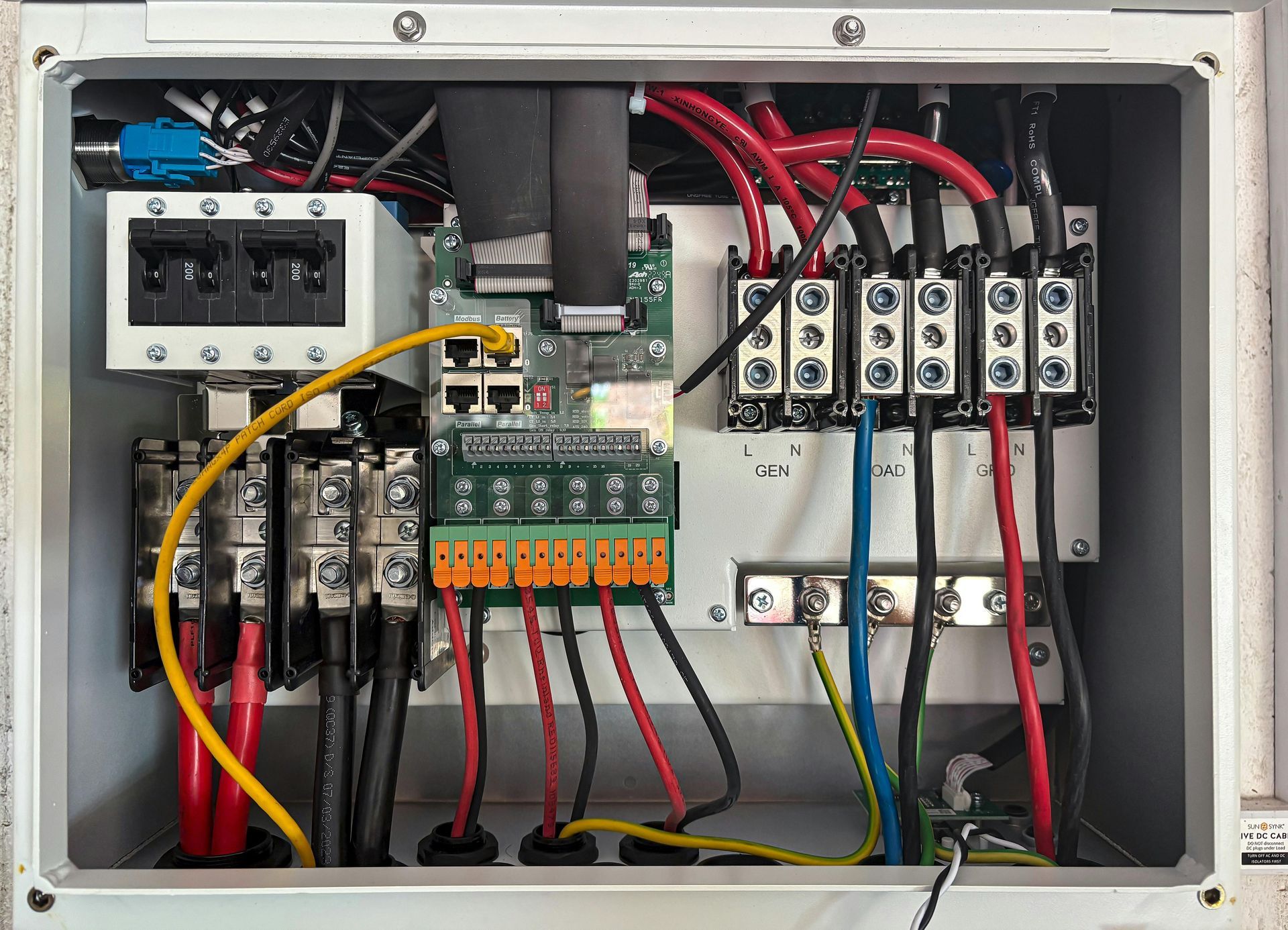 Electrical control panel with wires of various colors, terminal blocks, and circuit breakers inside a metal enclosure.