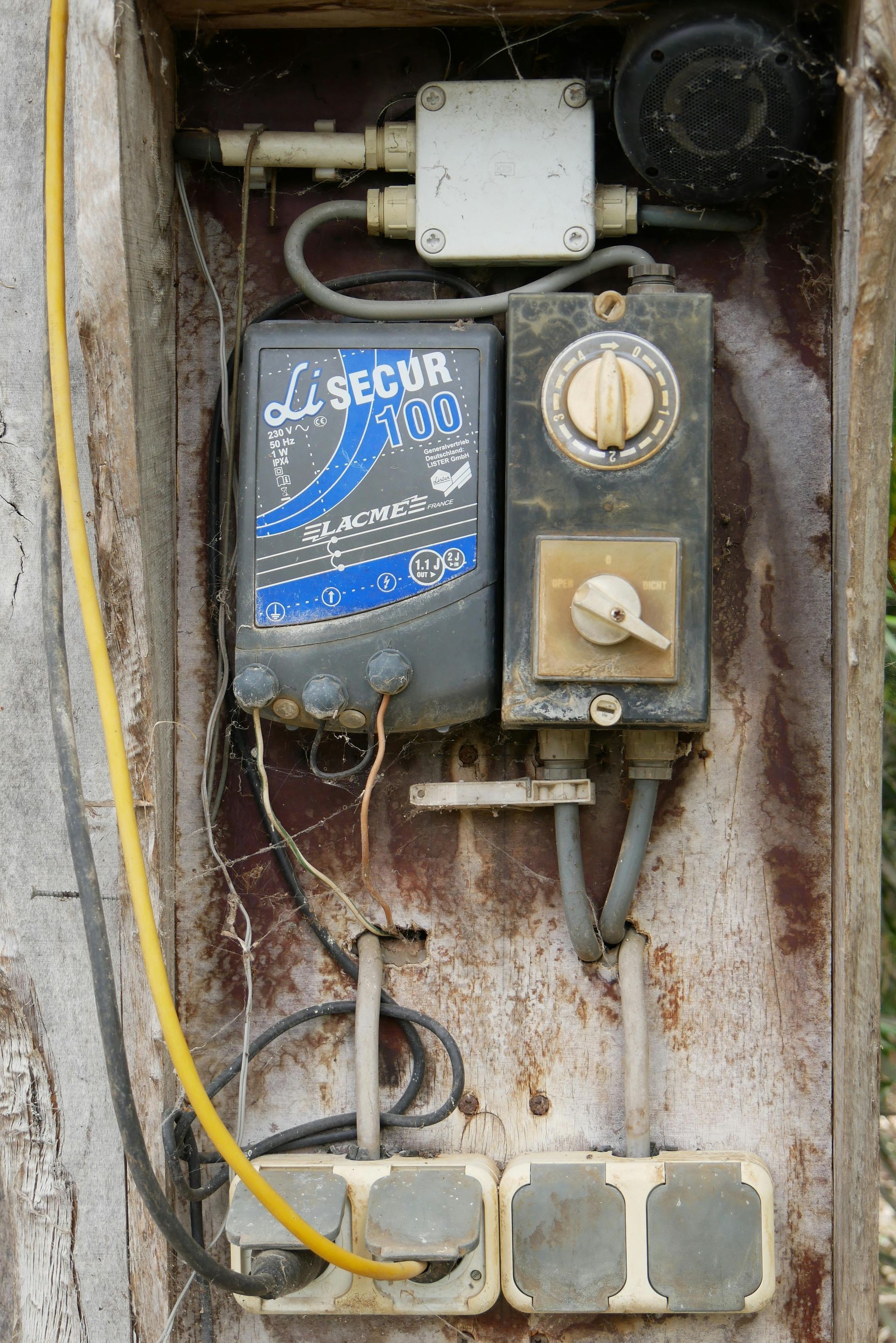 Weathered outdoor electrical panel with switches, outlets, and wiring.