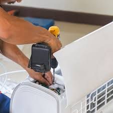 A technician uses a power drill to repair an open indoor air conditioning unit.