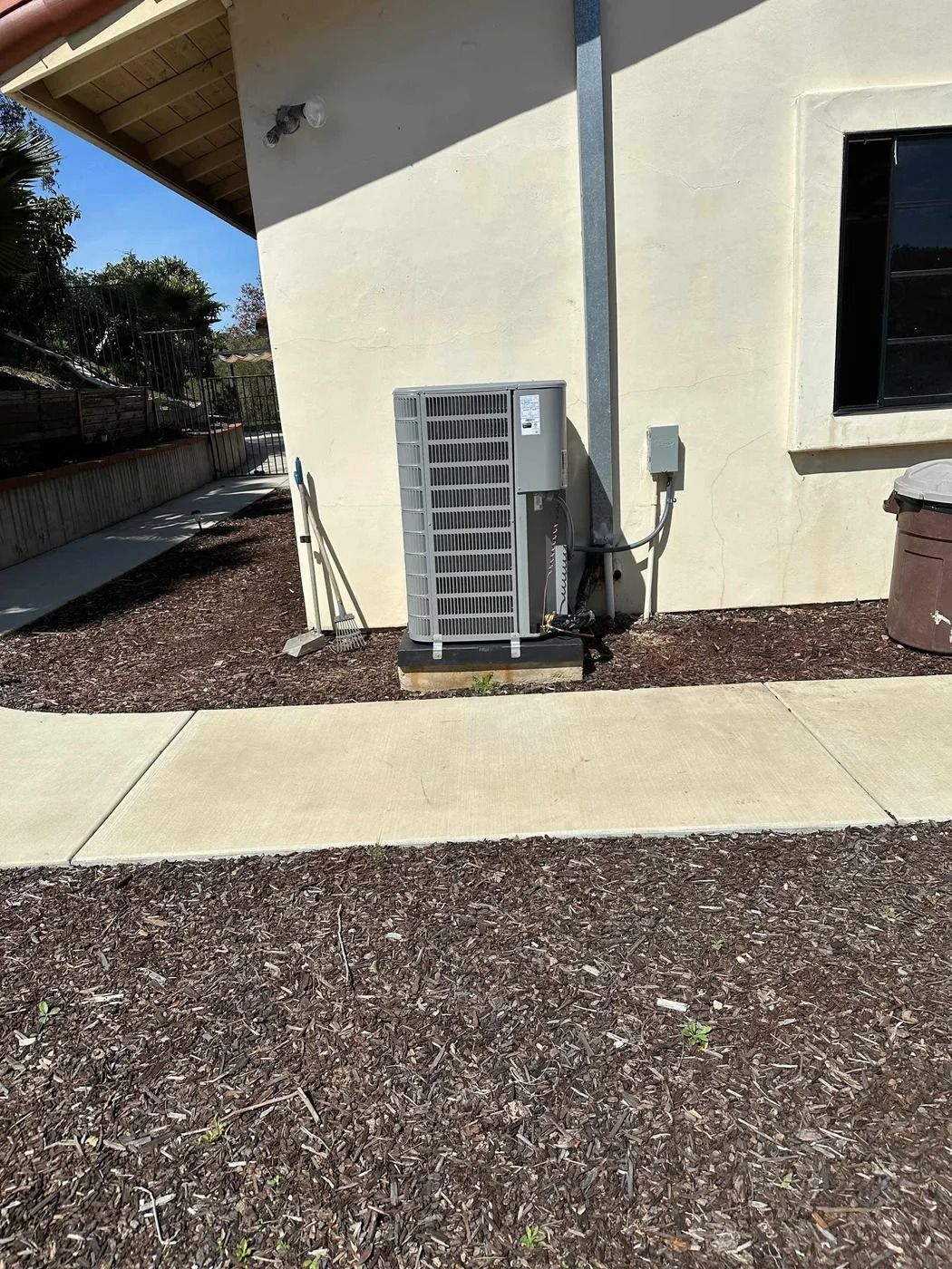 A large air conditioner is sitting on the side of a building next to a sidewalk.