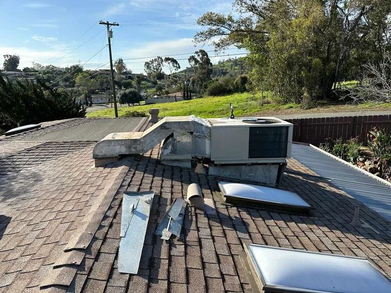 A roof with a broken air conditioner and a skylight on it.